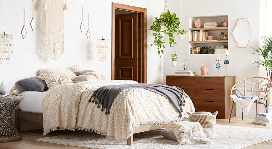 A bohemian minimalist bedroom with layered textures like a woven duvet cover and macrame wall hanging. Links to boho minimalism furniture & decor.